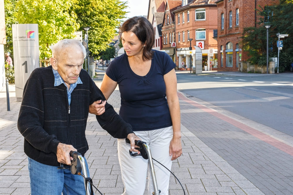 Pflegerin stützt einen Mann am Rollator