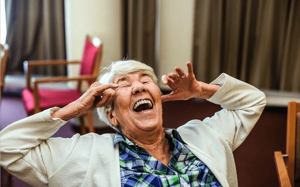 Seniorin lacht aus vollem Hals, auf einem Stuhl sitzend