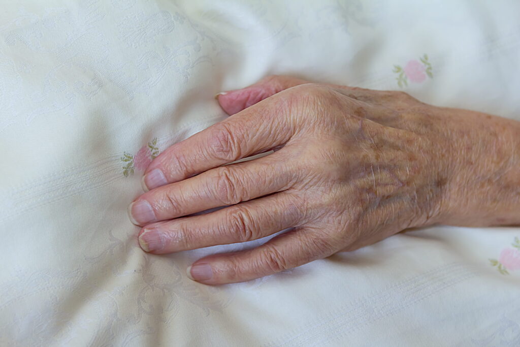 Hand älterer Frau über der Bettdecke