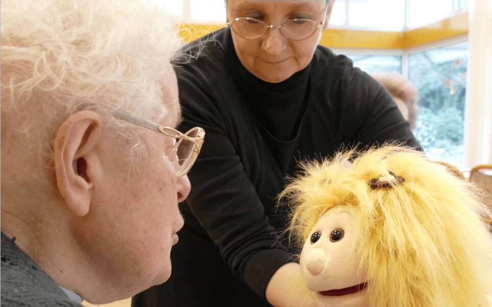 Seniorin freut sich an Handpuppe auf ihrem Schoß