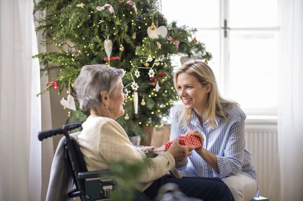 Seniorin erhält Geschenk unterm Weihnachtsbaum, Foto: AdobeStock/halfpoint