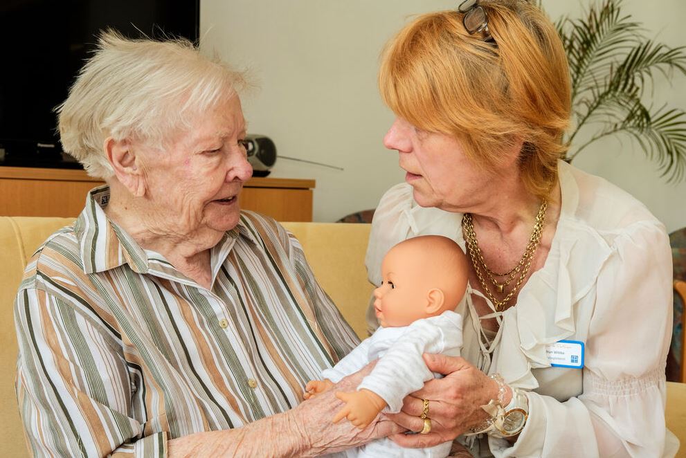 Seniorin und Betreuerin mit Babypuppe