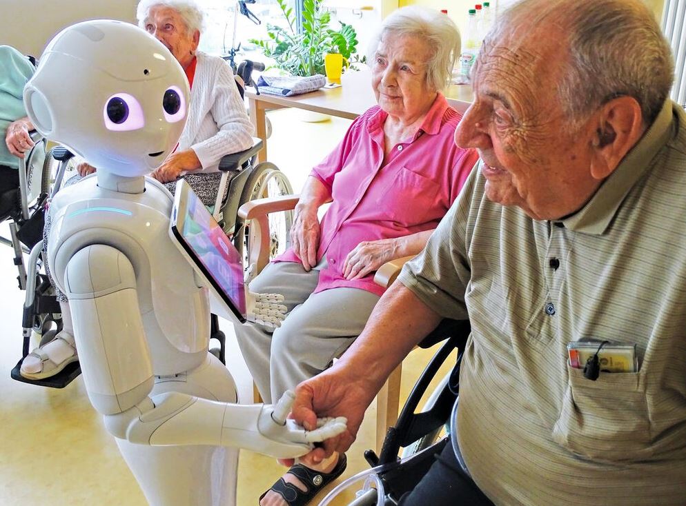 Roboter Pepper reicht Senior die Hand.