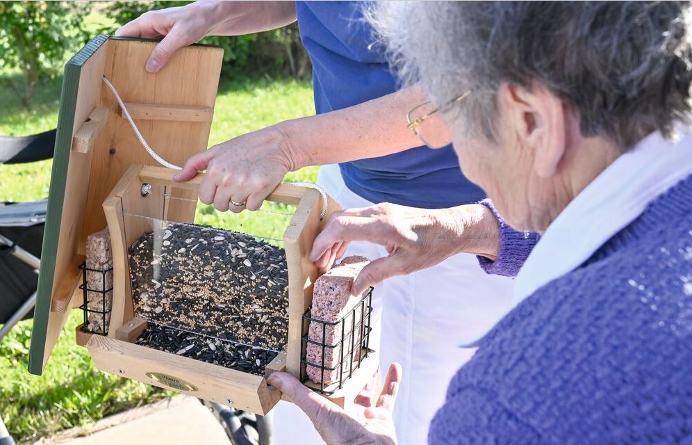 Seniorin füllt Vogelfutterstation
