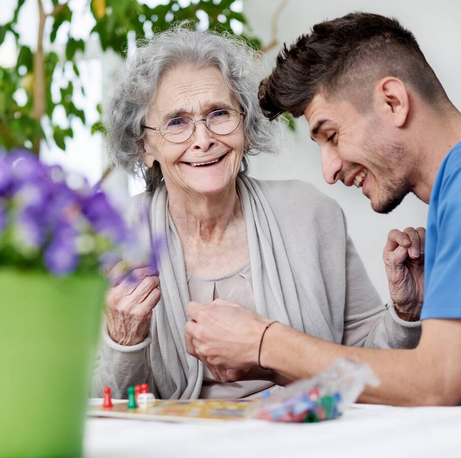 junger Mann und Seniorin spielen Mensch-ärgere-dich-nicht