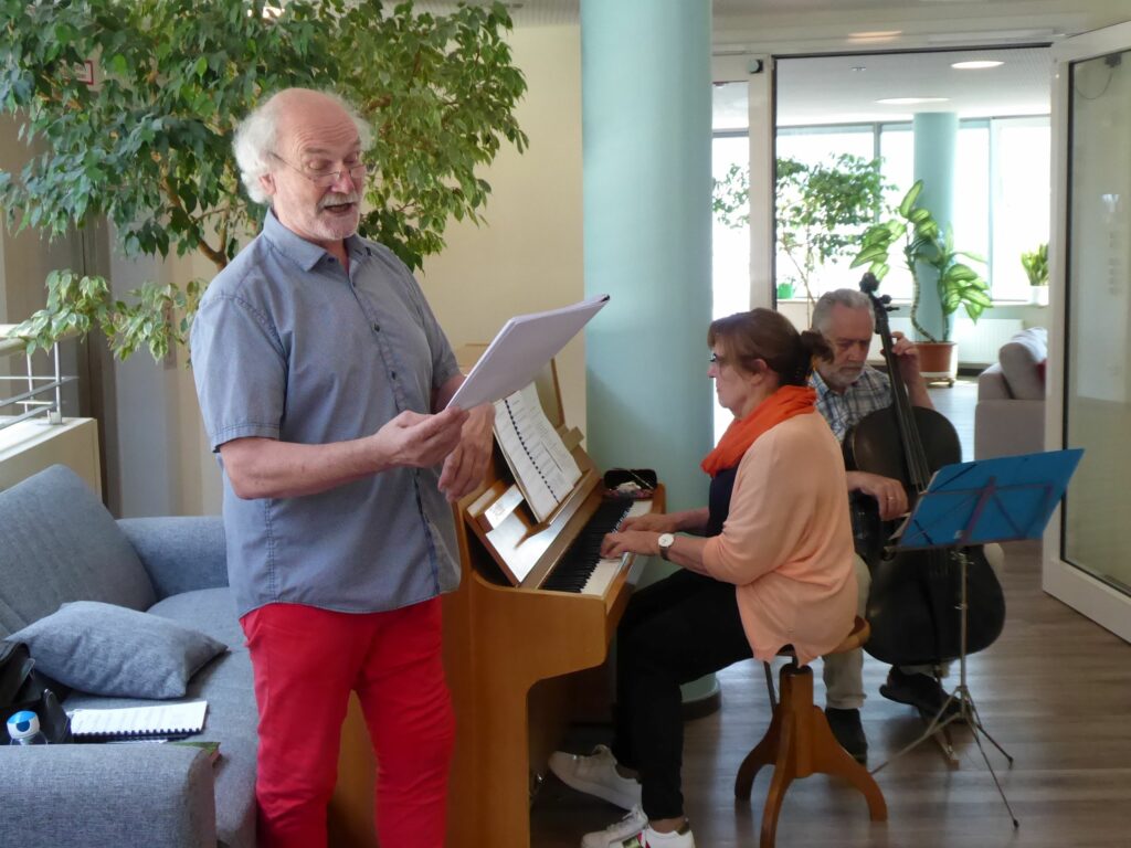 Mit Freude bei der Sache: Sowohl die Musikerinnen als auch die Gäste erfreuen sich jede Woche an der Live-Musik im Franziskuszentrum Friedrichshafen. Zu den ehrenamtlich aktiven Musizierenden gehören (v. l.) Sänger Peter Strecker, Elisabeth Raither-Hässler am Klavier und Johannes Becher am Cello.