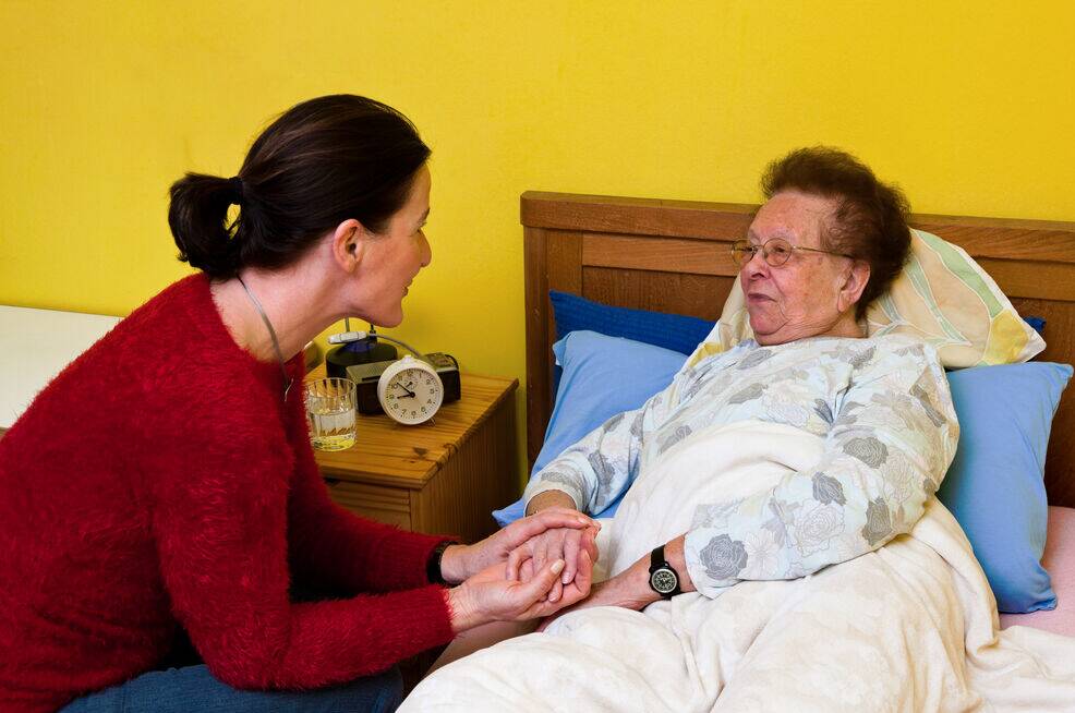 Junge Frau hält Seniorin im Bett die Hand