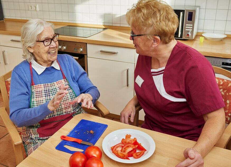 Seniorin und Betreuerin schneiden Tomaten
