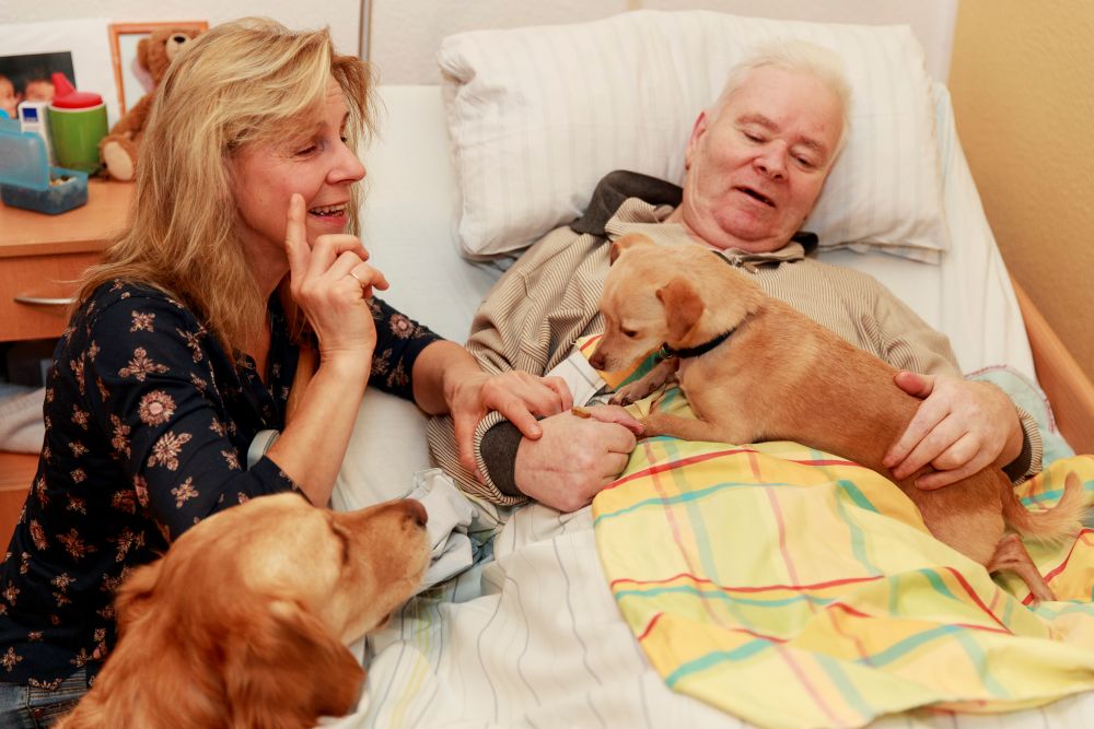 Betreuerin mit Hunden beim Bewohner im Bett
