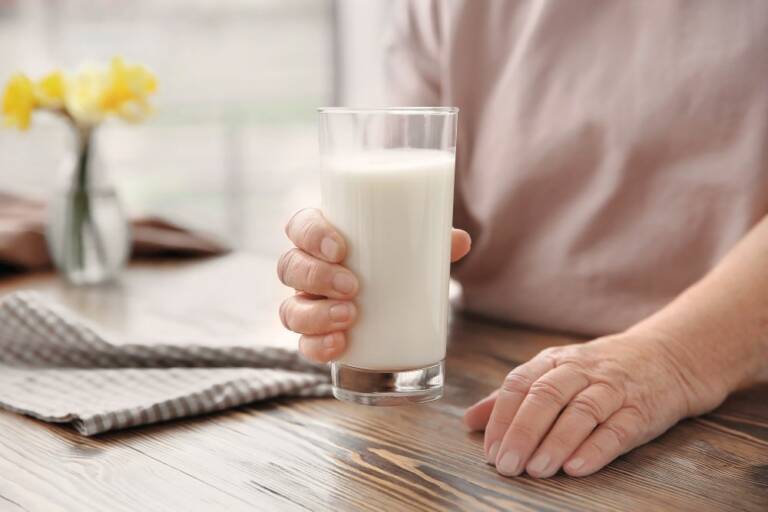 Seniorin mit einem Glas Buttermilich in der Hand